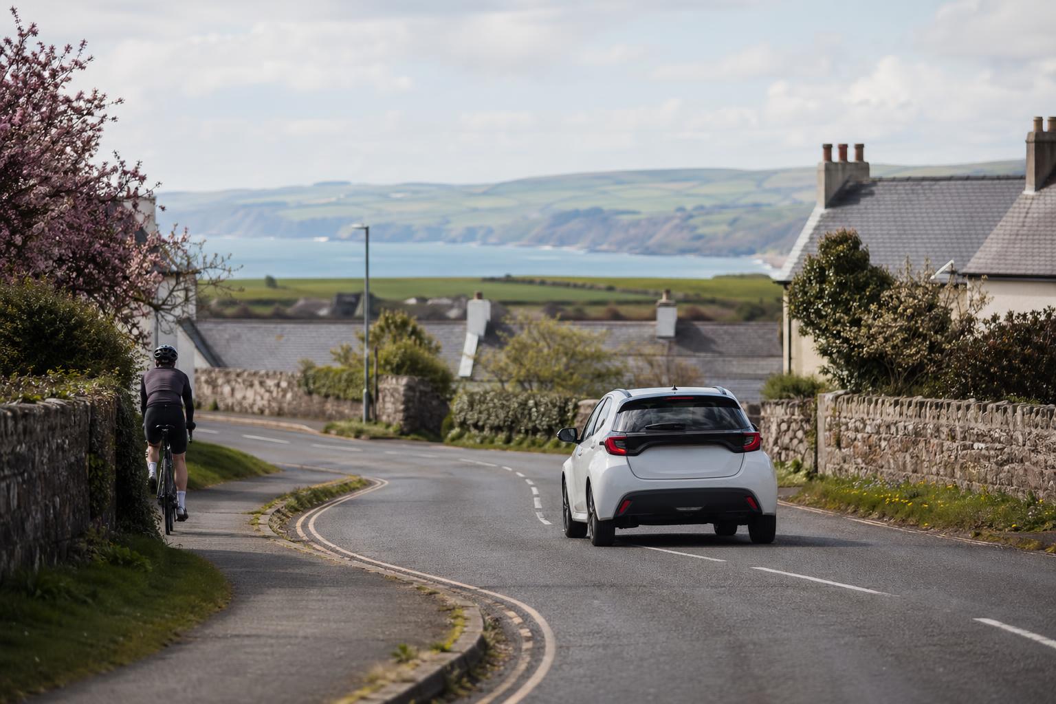 Compact car driving along a village-edge road with coastal hills near Braunton